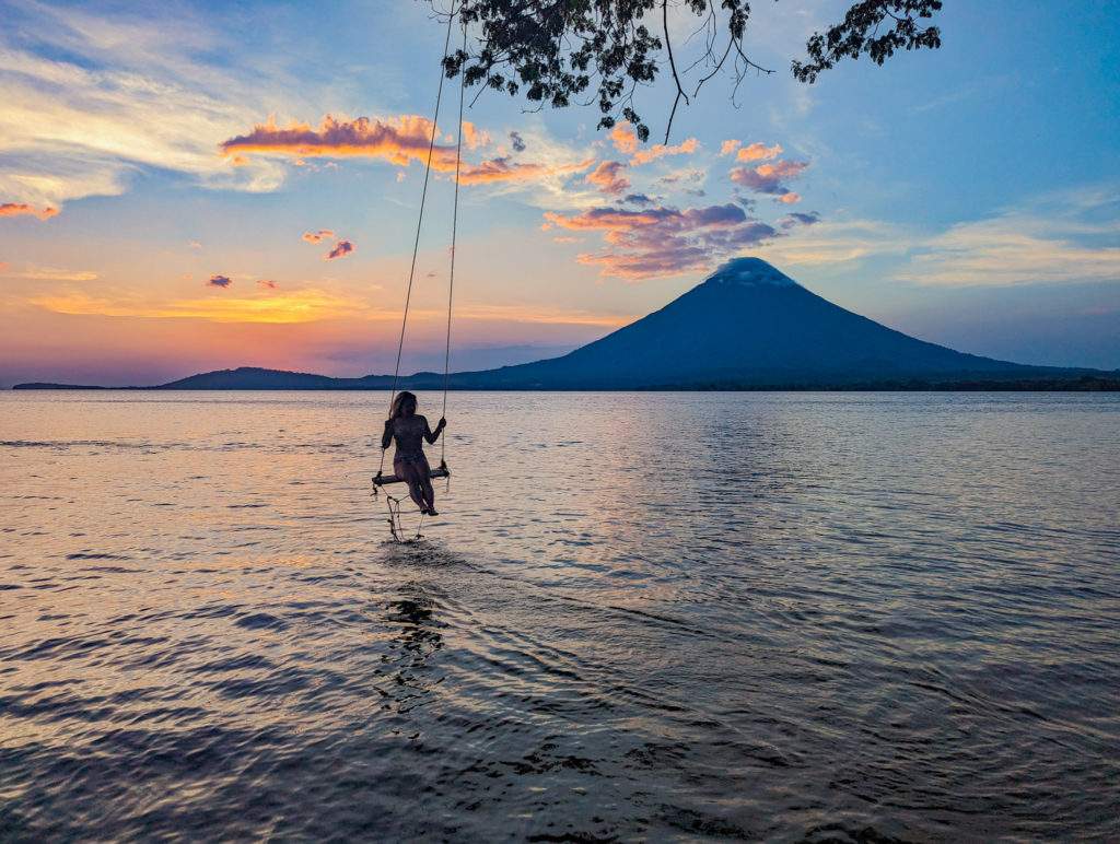 A woman swings over Lake Nicaragua during sunset with Volcan Concepcion visible in the background in Isla de Ometepe.