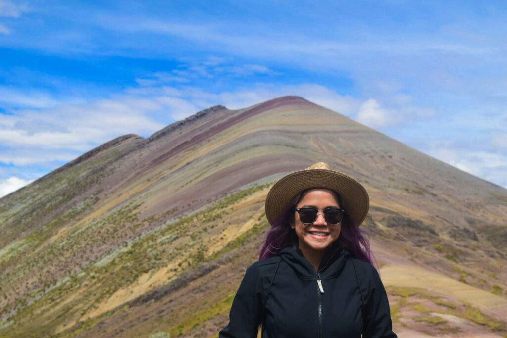 A woman stands in front of the first rainbow mountain in Palcoyo, Peru