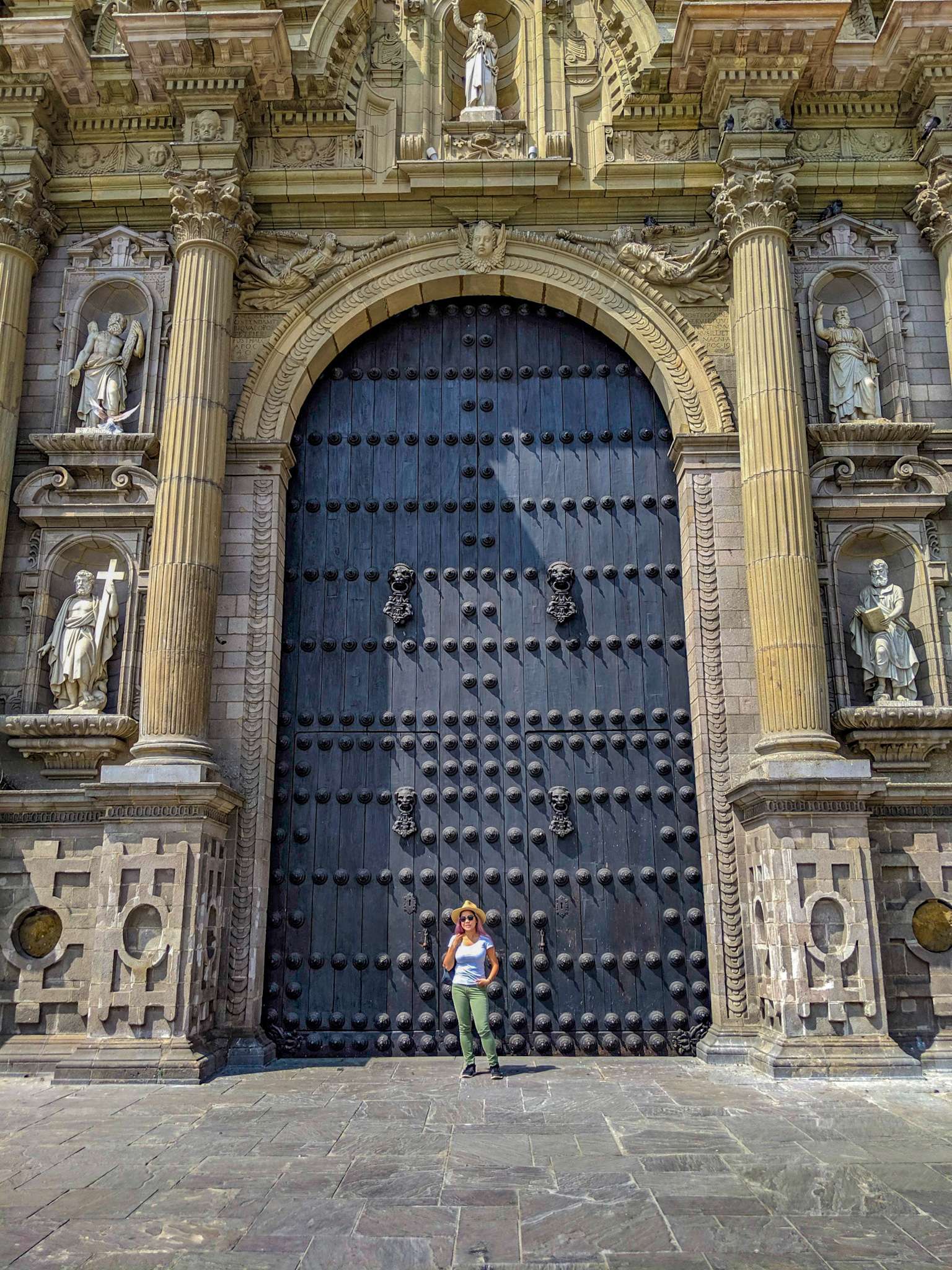A woman stands in front of the ancient, blue doors of the Lima Cathedral in Peru.